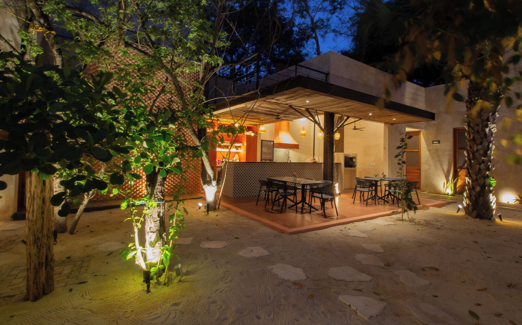 Un área de comedor al aire libre con un porche cubierto, piso de piedra y una zona de bar con asientos.