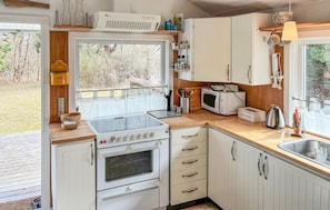 Una cocina con armarios blancos, estufa, microondas y ventana con vista a un patio.