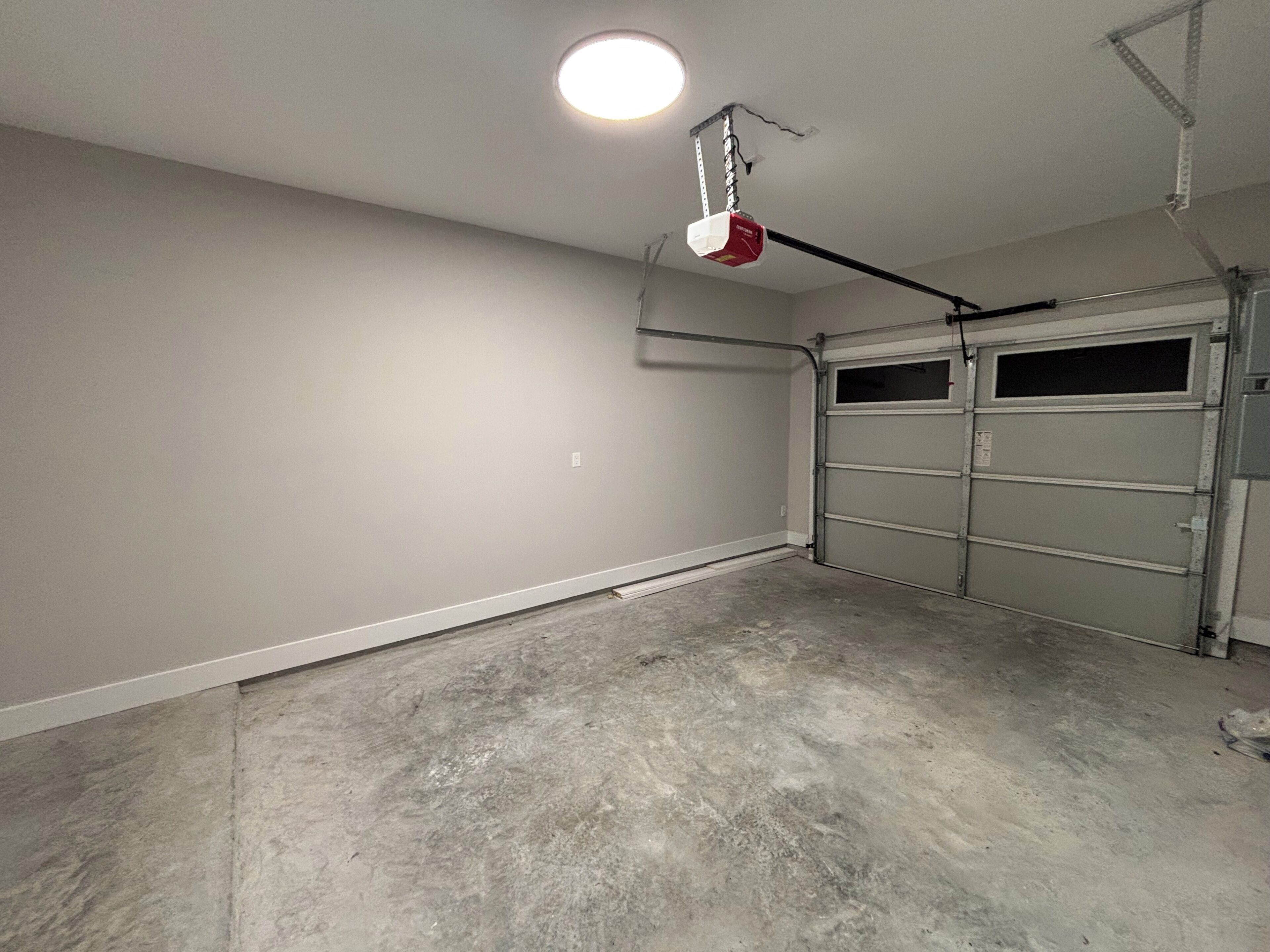 Un garage avec un sol en béton, un mur blanc et une porte de garage.