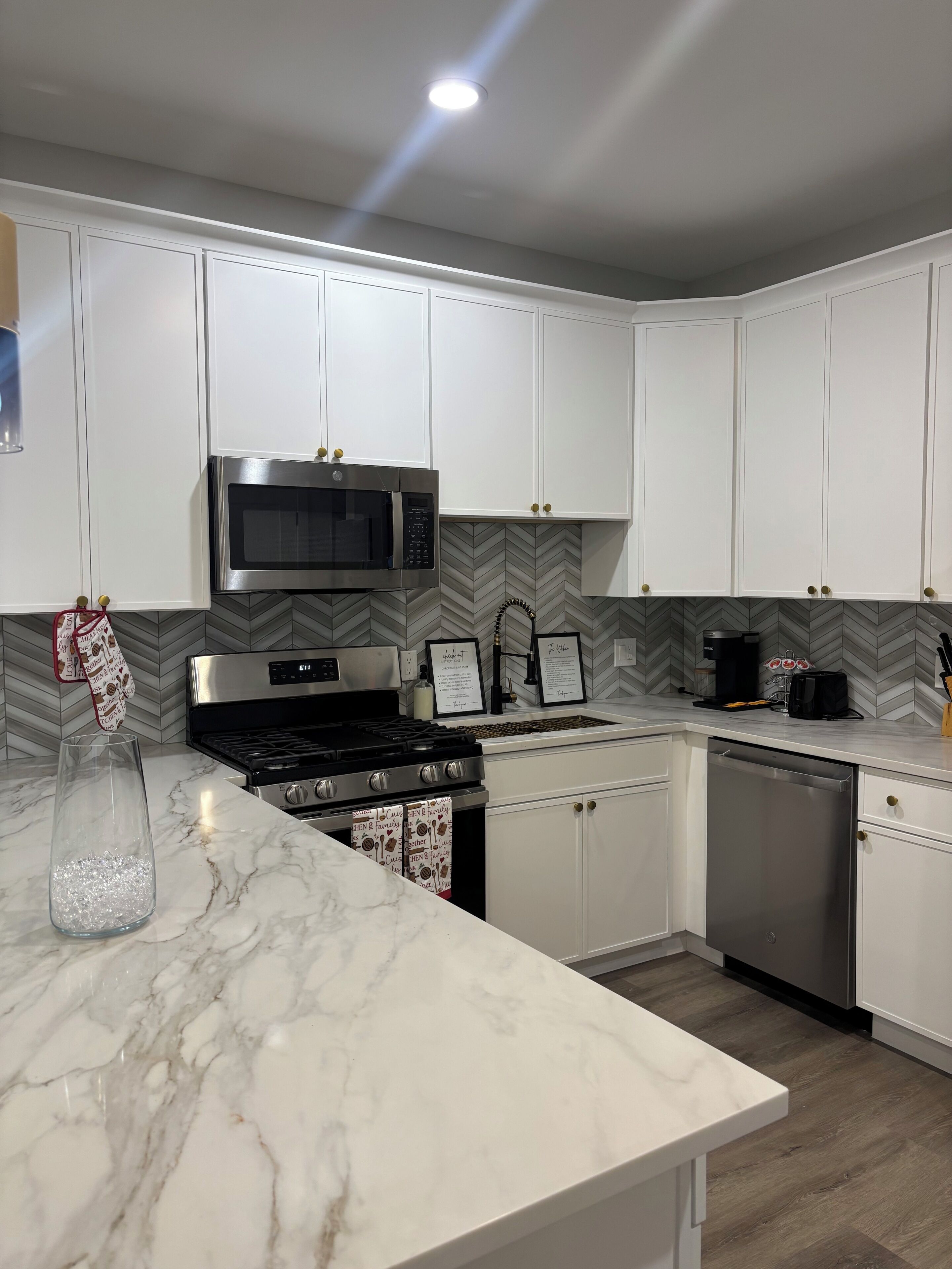 Una cocina moderna con gabinetes blancos, estufa de acero inoxidable, microondas y lavavajillas.