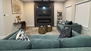 Ein Wohnzimmer mit Deckenventilator, Flachbildfernseher, Bücherregal und einem grünen Sofa.
