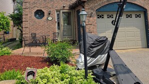 Une maison à deux étages, construite en briques, avec un garage, un patio couvert aménagé avec du mobilier d’extérieur et un lampadaire.