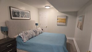 Une chambre à coucher avec un lit, une table de chevet, une lampe et des œuvres d’art encadrées accrochées aux murs.