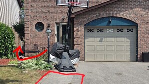 Une maison d’habitation avec une façade en briques, une porte de garage et un panier de basketball installé dans l’allée.