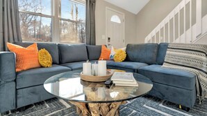 A modern living room with a sectional sofa, a glass coffee table, and a view of the outdoors. - Hot Tub, Jungle Gym, Fire Pit - Private Cabin Gem! (Tobyhanna)