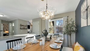 A dining area with a wooden table set for four, a chandelier, and a view of the outside. - Hot Tub, Jungle Gym, Fire Pit - Private Cabin Gem! (Tobyhanna)