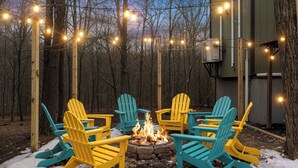 A fire pit with chairs arranged around it, surrounded by trees and a building structure. - Hot Tub, Jungle Gym, Fire Pit - Private Cabin Gem! (Tobyhanna)