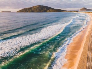 Une plage avec des vagues, une rive sablonneuse et des collines à l’horizon.