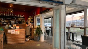 An indoor bar area with a wooden counter, a potted plant, and a view through a glass door to the outside. - Hawks Nest Hideaway | Spa, BBQ, Bikes & Pool Table (Hawks Nest)