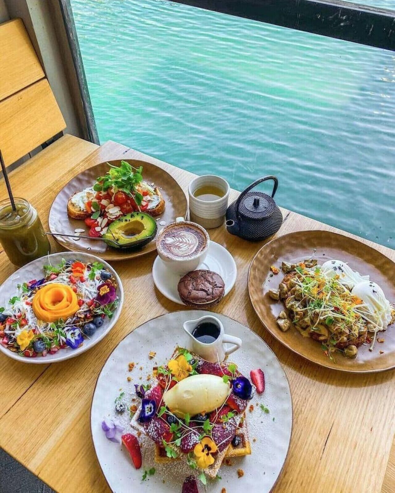 A table with various dishes and a teapot, set against a view of water.