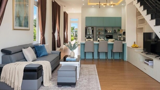 Una sala de estar moderna con sofá, reposapiés y un comedor con sillas, y una cocina al fondo.