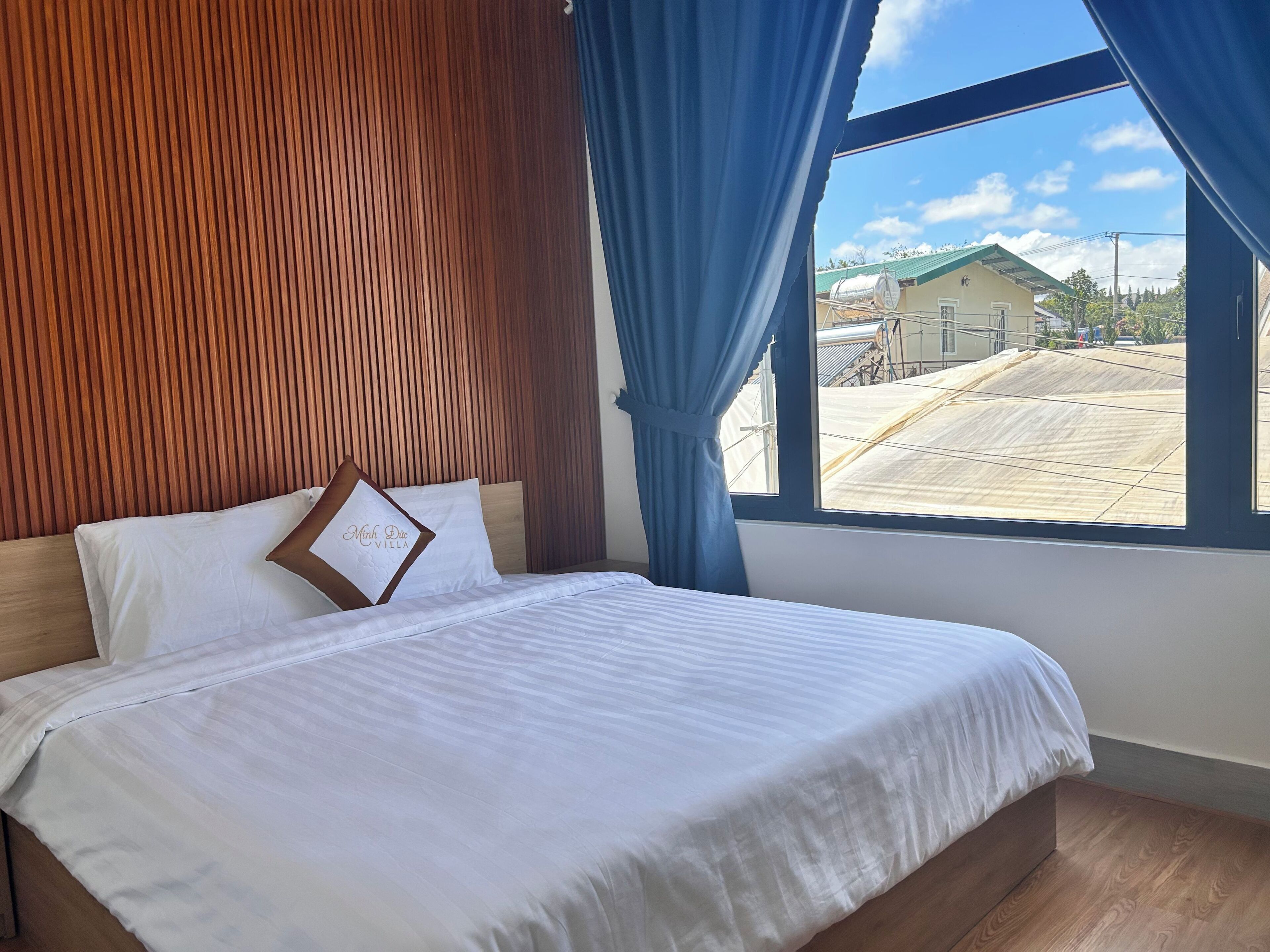 A bedroom with a wooden headboard, a bed with white bedding, and a view of a building through a window.