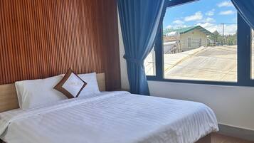 A bedroom with a wooden headboard, a bed with white bedding, and a view of a building through a window.