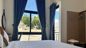 Habitación de hotel con cama, armario de madera, perchero y vistas al exterior.