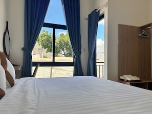 A hotel room with a bed, a wooden wardrobe, a hanging coat rack, and a view of the outside.