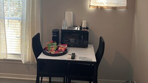 Zona pranzo con tavolo, sedie, forno a microonde, cestino e finestra con tende.
