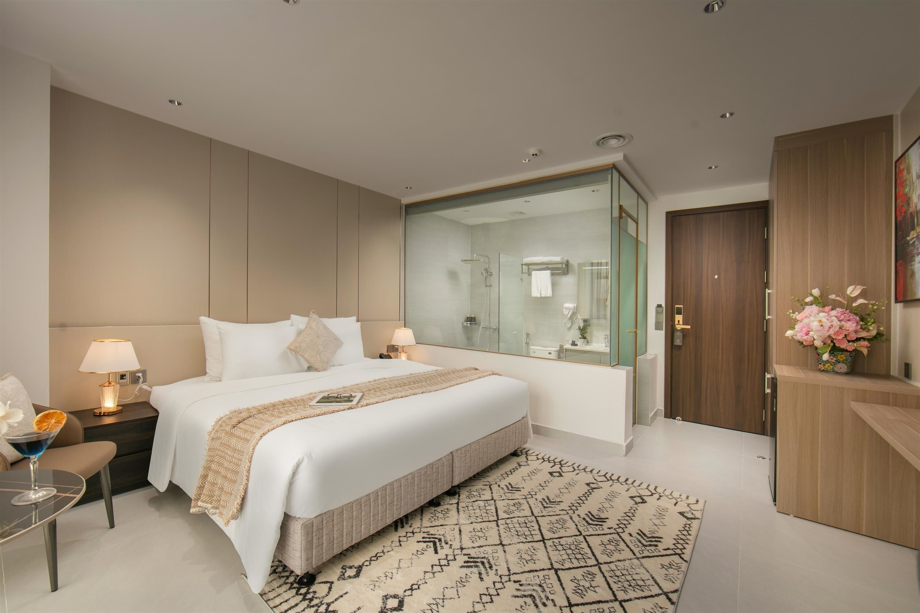 Une chambre d’hôtel moderne avec un grand lit, des tables de chevet avec des lampes, une douche en verre et une armoire en bois.
