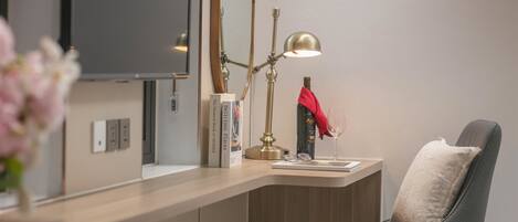 Una habitación moderna con escritorio, silla, lámpara, espejo y un jarrón con flores.