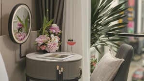 Una camera moderna con un tavolo rotondo, uno specchio, un vaso con fiori, un drink e vista sulla città.