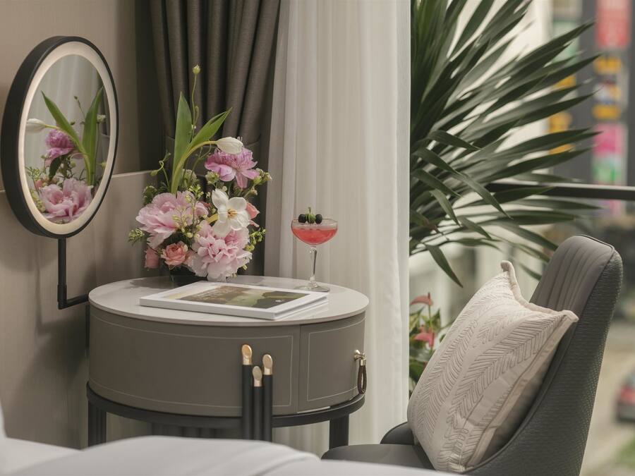 A modern room with a round table, a mirror, a vase with flowers, a drink, and a view of the city.