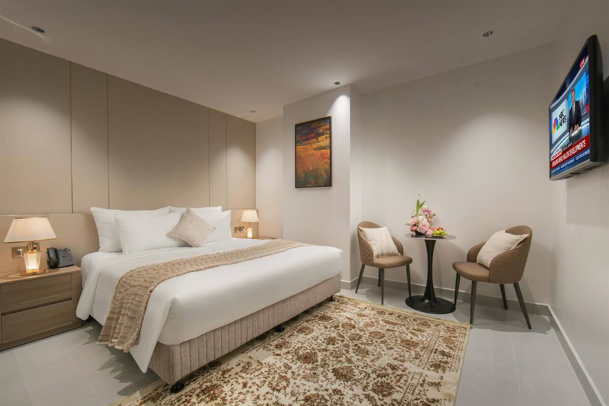Une chambre d’hôtel moderne avec un grand lit, des lampes de chevet, un téléviseur à écran plat, une petite table agrémentée de fleurs et deux chaises.