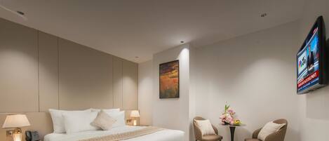 A modern hotel room with a large bed, bedside lamps, a flat-screen TV, a small table with flowers, and two chairs.