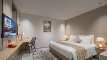 A hotel room with a bed, bedside table, lamp, chair, TV displaying NBC News, and a fruit tray.