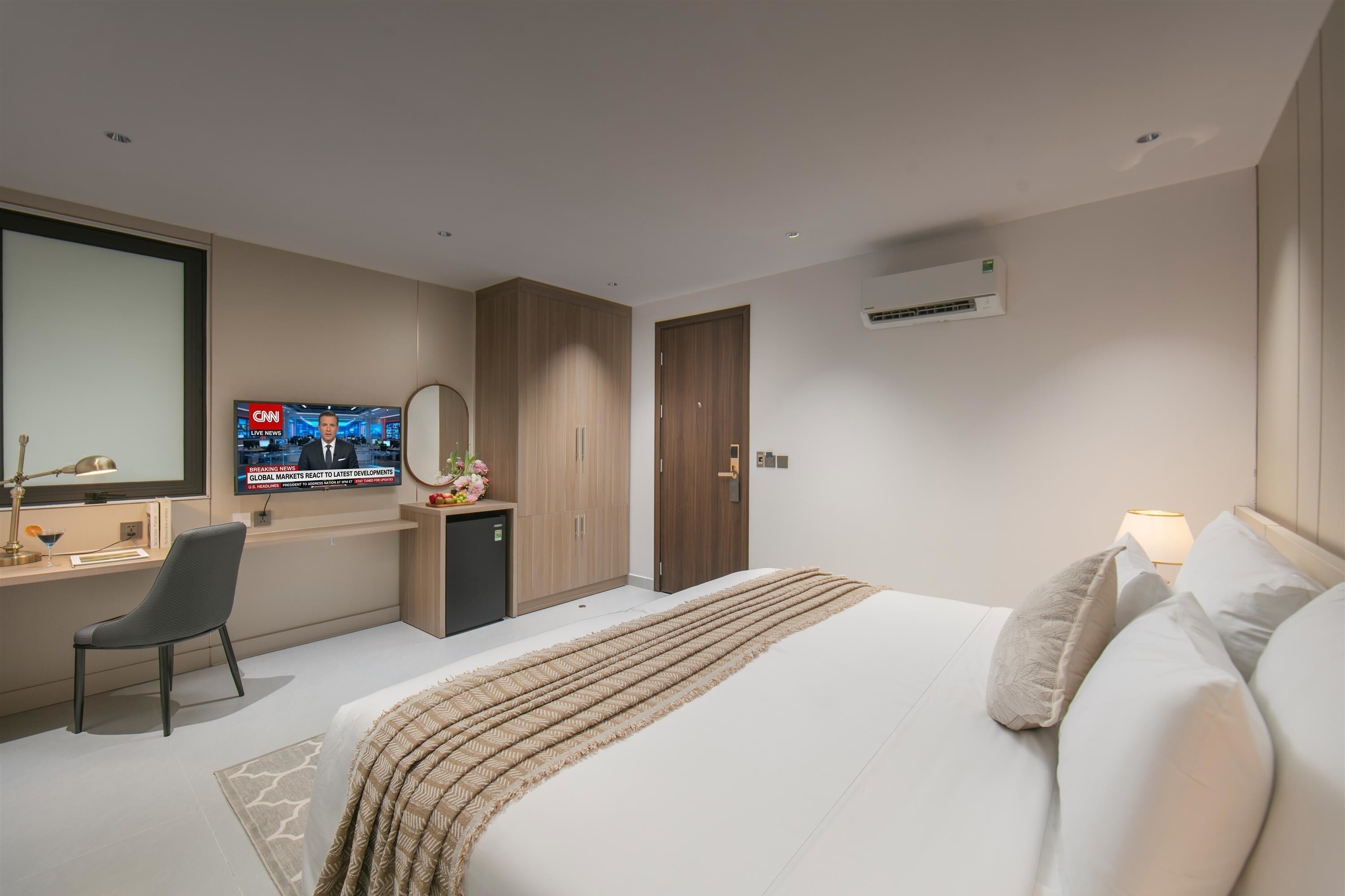 A hotel room with a bed, a desk with a chair, a television, and an air conditioning unit.
