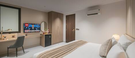 A hotel room with a bed, a desk with a chair, a television, and an air conditioning unit.