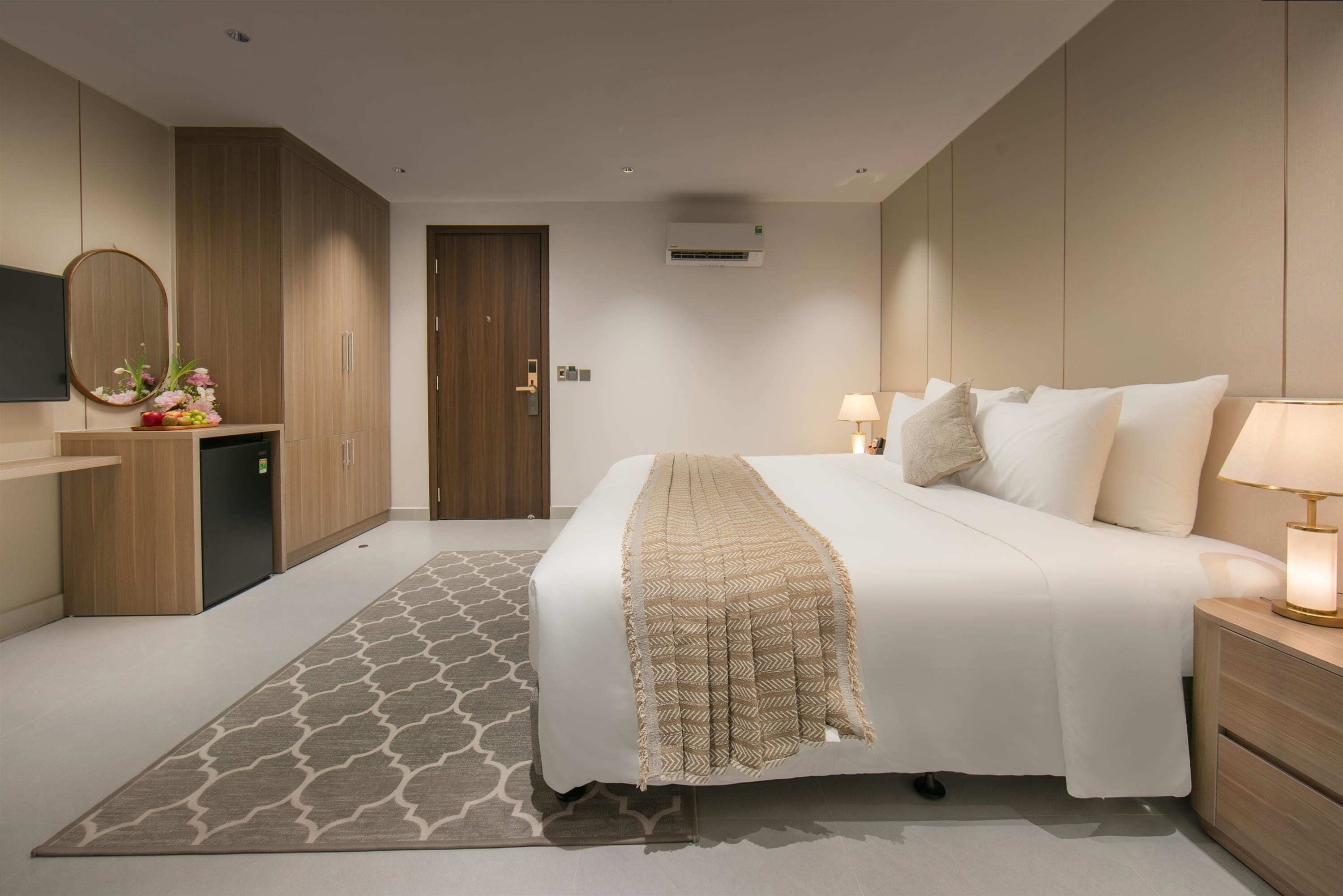 Una habitación de hotel con cama, mesitas de noche, televisor, armario y alfombra estampada.