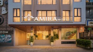 Un hotel moderno con un segno ben visibile AMIRA HOTEL, un ingresso centrale con gradini e ampie finestre.