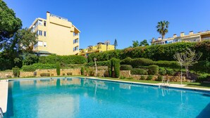 A swimming pool with clear blue water, surrounded by well-maintained hedges and a stone wall. - Moon Beach Garden View (Mijas)
