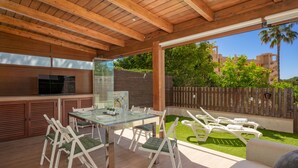 An outdoor patio with a wooden ceiling, a glass table, white chairs, a sofa, and a view of a residential area. - Moon Beach Garden View (Mijas)