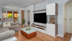 A modern living room with a flat-screen TV, a sofa, a coffee table, and a TV stand with decorative items. - Moon Beach Garden View (Mijas)