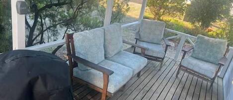A covered outdoor seating area with wooden deck flooring and light grey upholstered chairs.