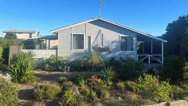 A single-story mobile home with a sloped roof, a satellite dish, and a fenced yard with various plants. - The Nest, Wifi - NO Pets (Robe)