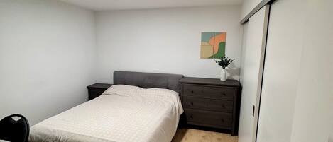 A bedroom with a bed, bedside table, chair, and a small desk.