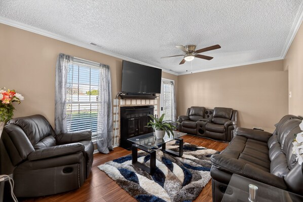 A living room with a fireplace, leather recliners, a glass coffee table, and a ceiling fan.