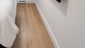 Un dormitorio con una cama, un televisor montado en la pared, una ventana y suelo de madera.