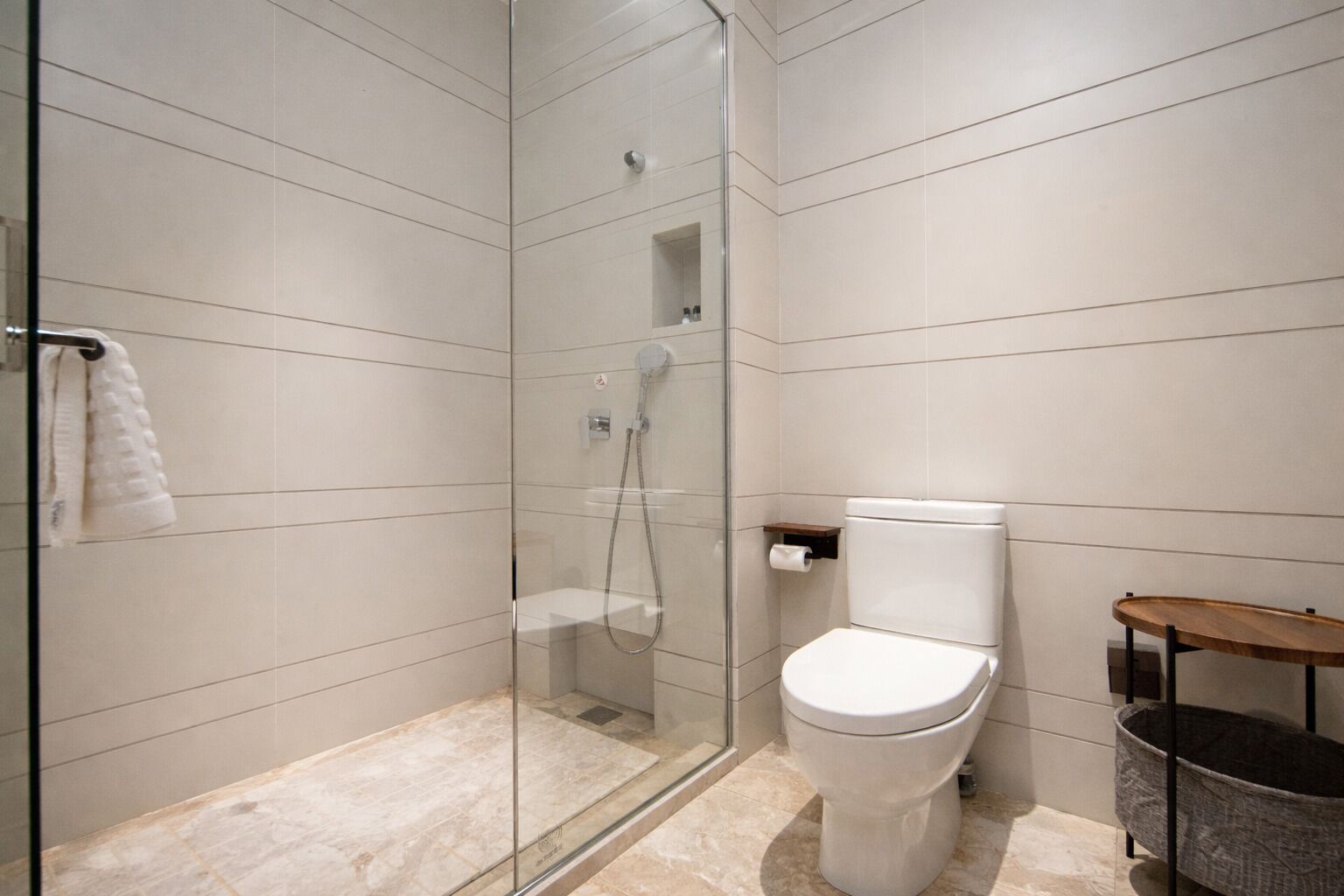 Un baño moderno con ducha de vidrio, inodoro y un pequeño estante de madera.