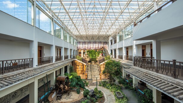 Ein geräumiger Innenhof mit Glasdach, einer zentralen Treppe und einem Gartenbereich.