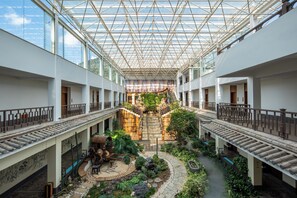 Un amplio atrio con techo de cristal, una escalera central y un jardín.