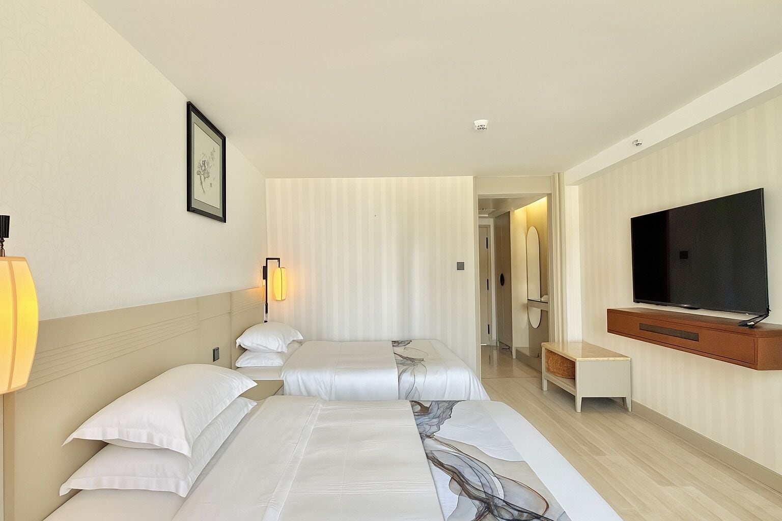 Una habitación de hotel con dos camas, televisión, lámpara de noche y espejo.