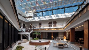 Ein geräumiger Innenhof mit Glasdecke, einer zentralen Sitzgruppe und einer Treppe.
