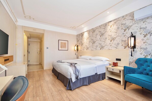 Una habitación de hotel con cama, mesita de noche, lámpara, sillón y televisor.
