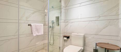 A modern bathroom with a glass-enclosed shower, a toilet, and a small wooden side table.