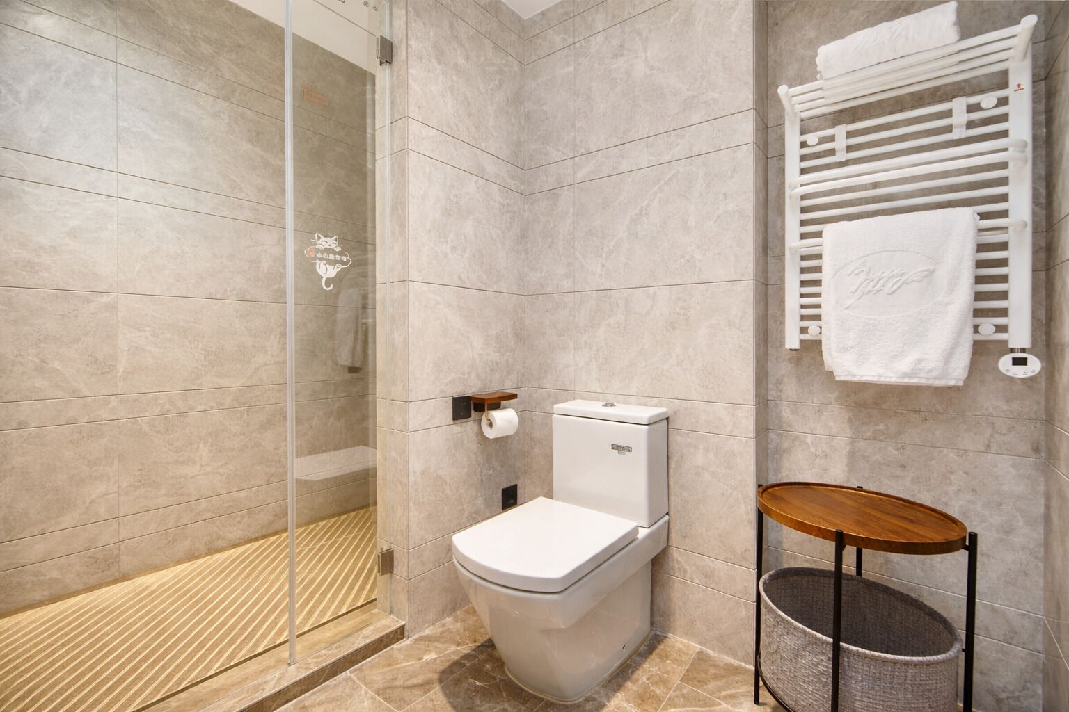 A modern bathroom with a glass shower enclosure, a toilet, a towel rack, and a small wooden stool.