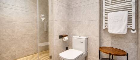 A modern bathroom with a glass shower enclosure, a toilet, a towel rack, and a small wooden stool.