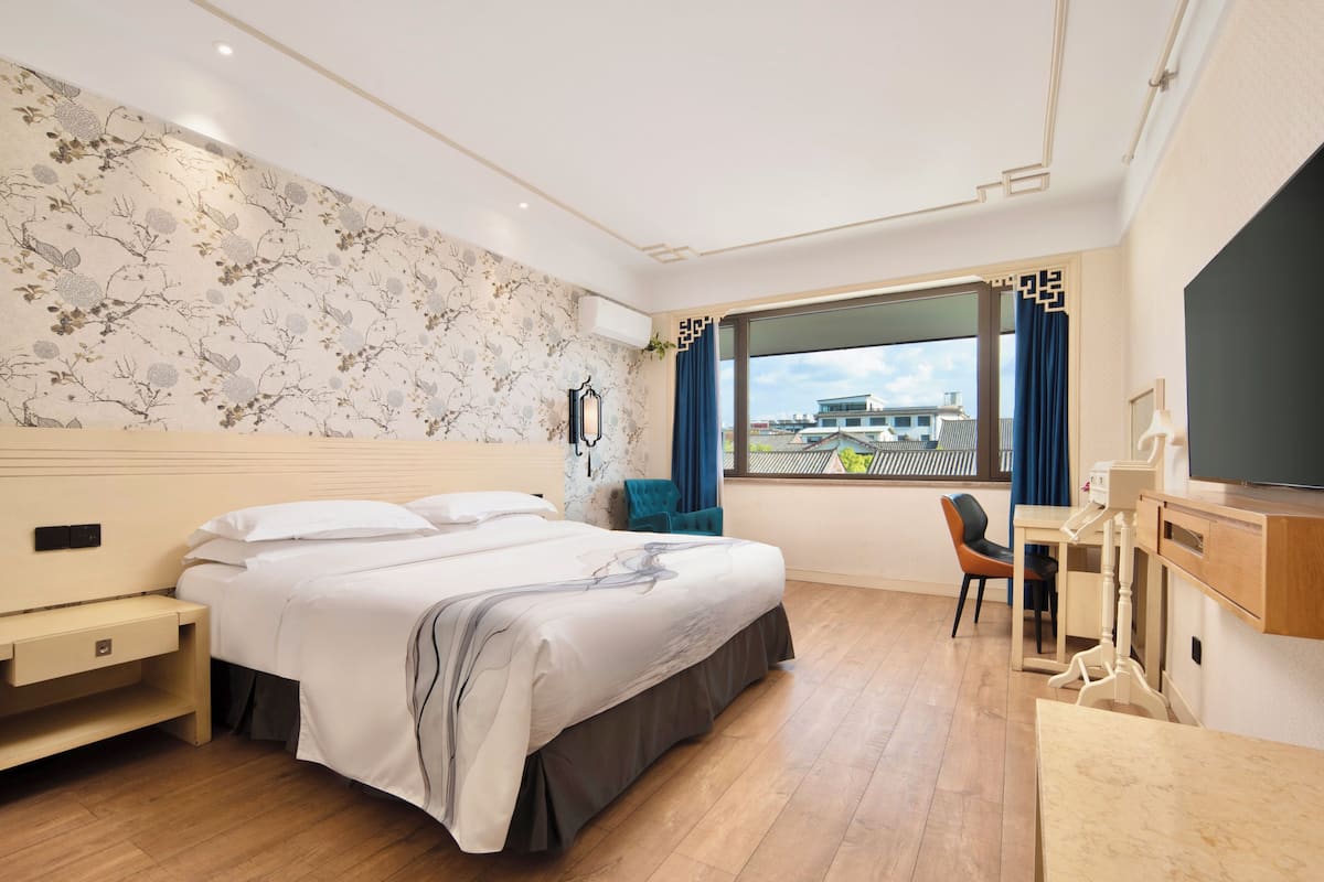 Een hotelkamer met een bed, bureau, stoel en een groot raam met uitzicht.