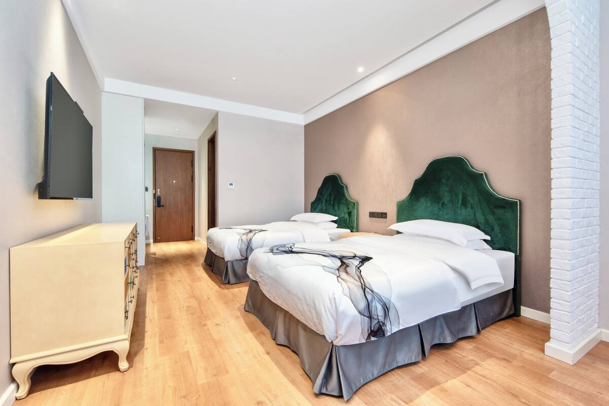 Een hotelkamer met drie bedden, een dressoir, een flatscreen televisie en een houten vloer.